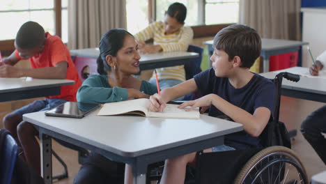 in school, teacher assisting student in wheelchair with writing in classroom