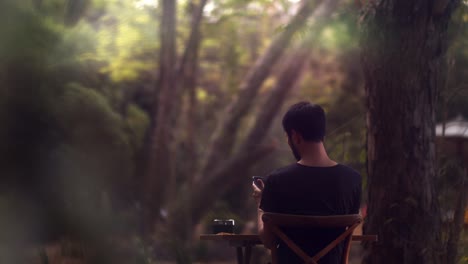 Asian-man-sitting-outside-in-the-garden-at-a-table-and-working-on-his-smartphone---cinematic-shot