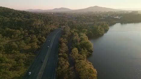 a dynamic aerial shot at a lower altitude flying over a multilane highway at sunrise. the early morning light casts long shadows, emphasizing the urban infrastructure and movement of traffic.