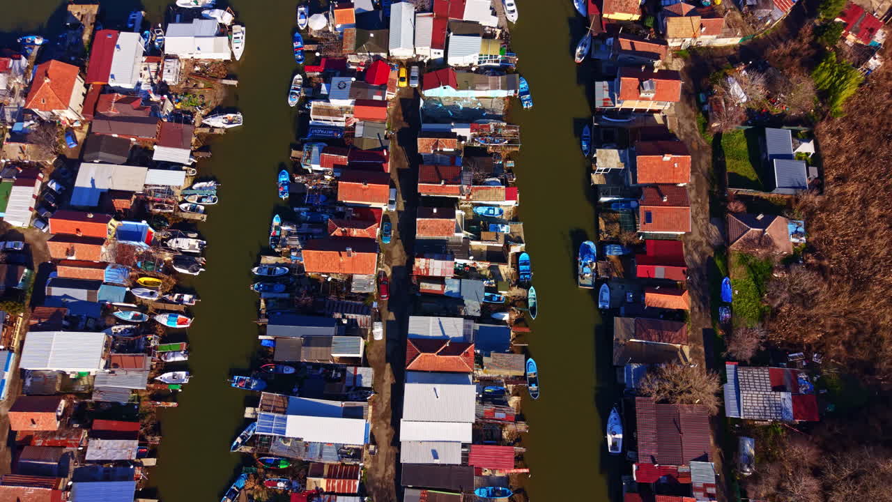Blick auf Boote und Häuser entlang eines Wasserwegs in einem kleinen Dorf mit schmalen Kanälen und festgemachten Schiffen, umgeben von Grün.