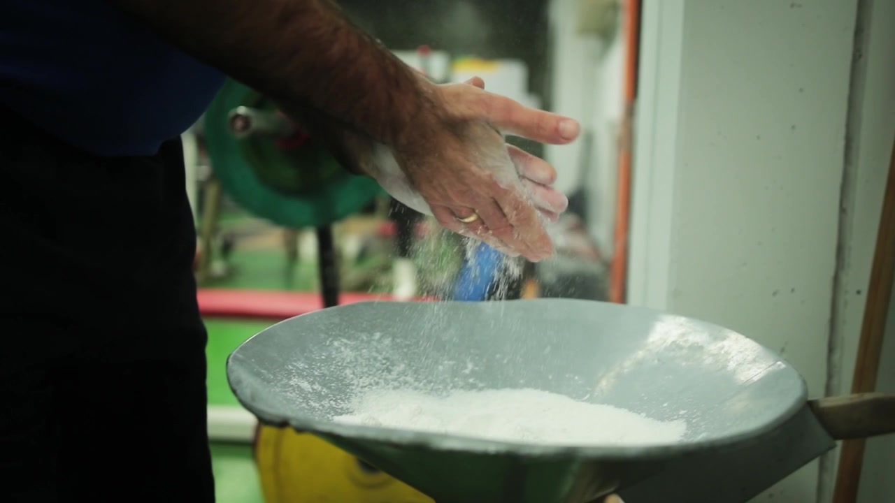 Primo piano a mano libera in slow motion, un pesista si strofina la polvere di magnesite sulle mani per migliorare la presa prima di una sessione di allenamento della forza, catturando la preparazione e la concentrazione in una palestra