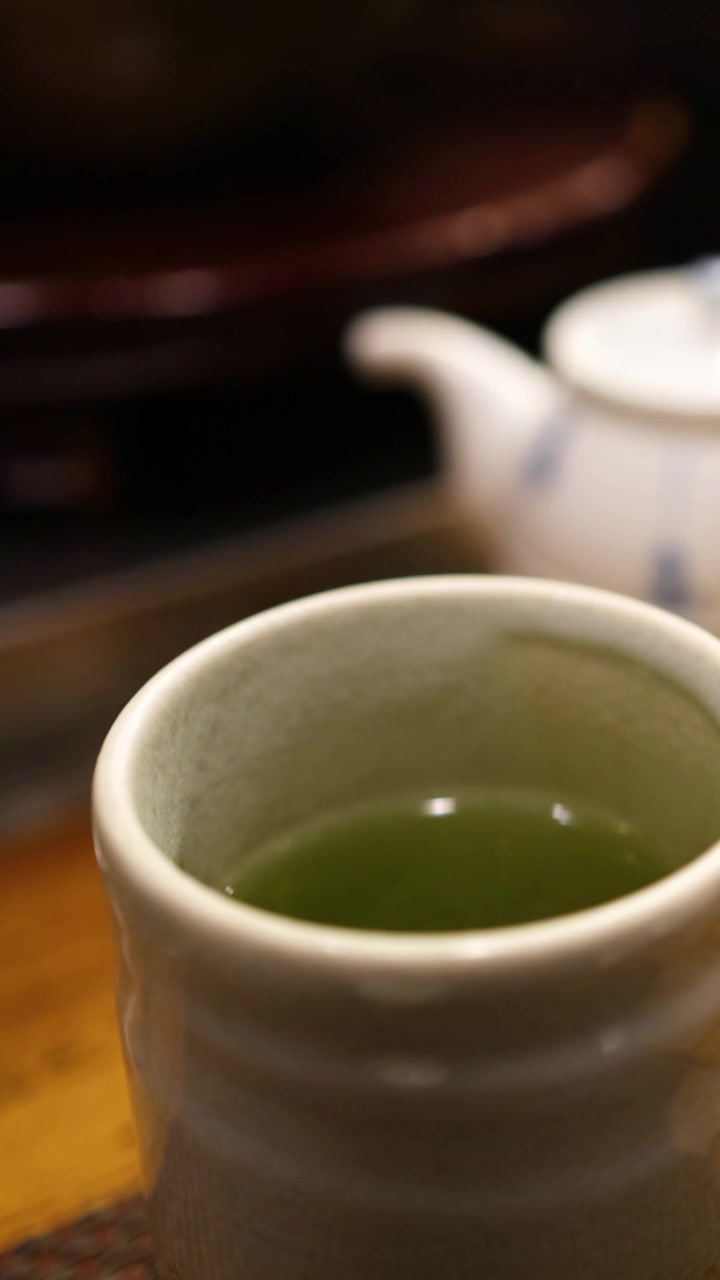 Un primo piano verticale di una tazza di ceramica piena di tè verde su un tavolo.
