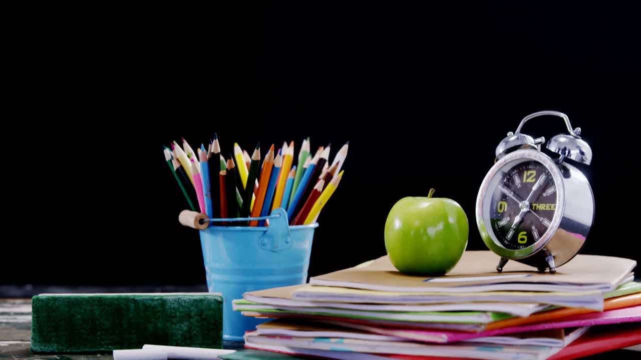 Apple and alarm clock on book stack with school supplies