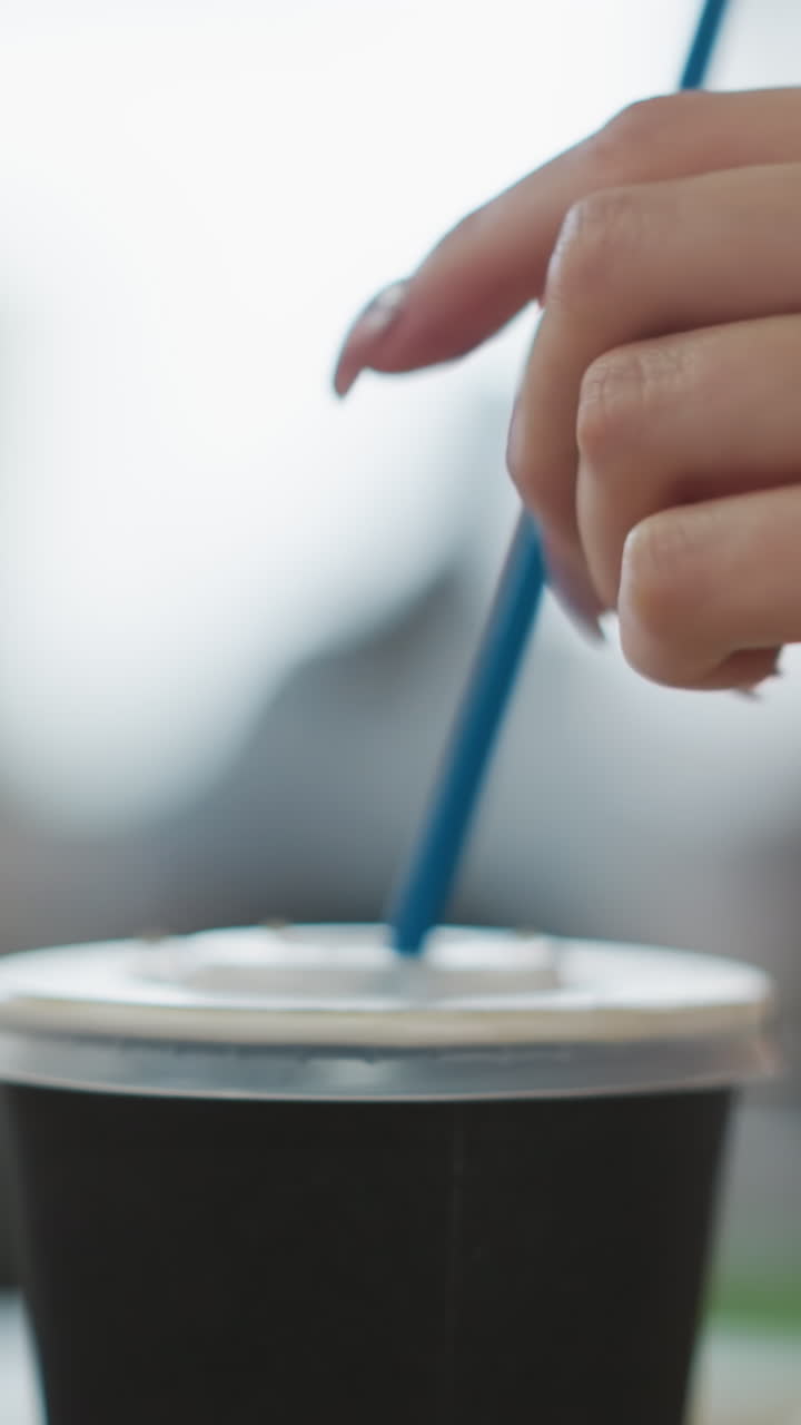 primer plano de la mano insertando suavemente paja azul en la tapa de la taza de café para llevar en un entorno interior vibrante con fondo borroso y luces bokeh brillantes, ilustrando la sostenibilidad y el estilo de vida moderno