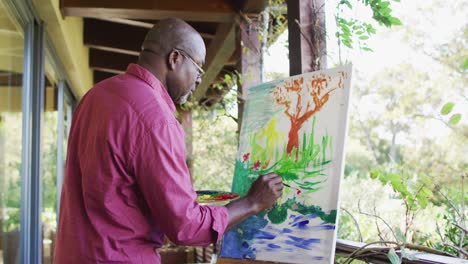 happy african american senior man standing on balcony painting picture of the view