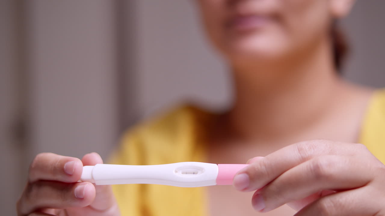 Blurry shot of a smiling expectant pregnant woman holding a pregnancy test kit, showing a positive result