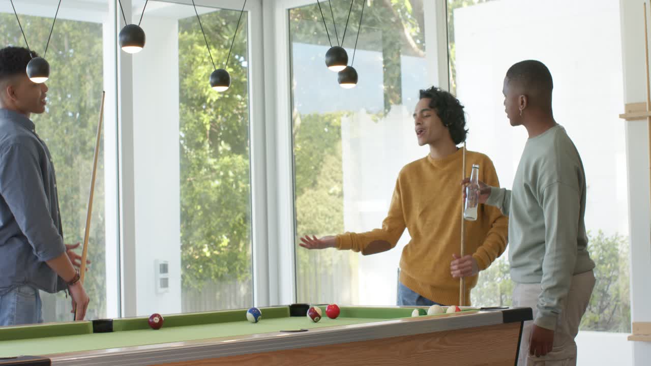 Diverse male friends lining up shot then debating strategy at pool table near windows