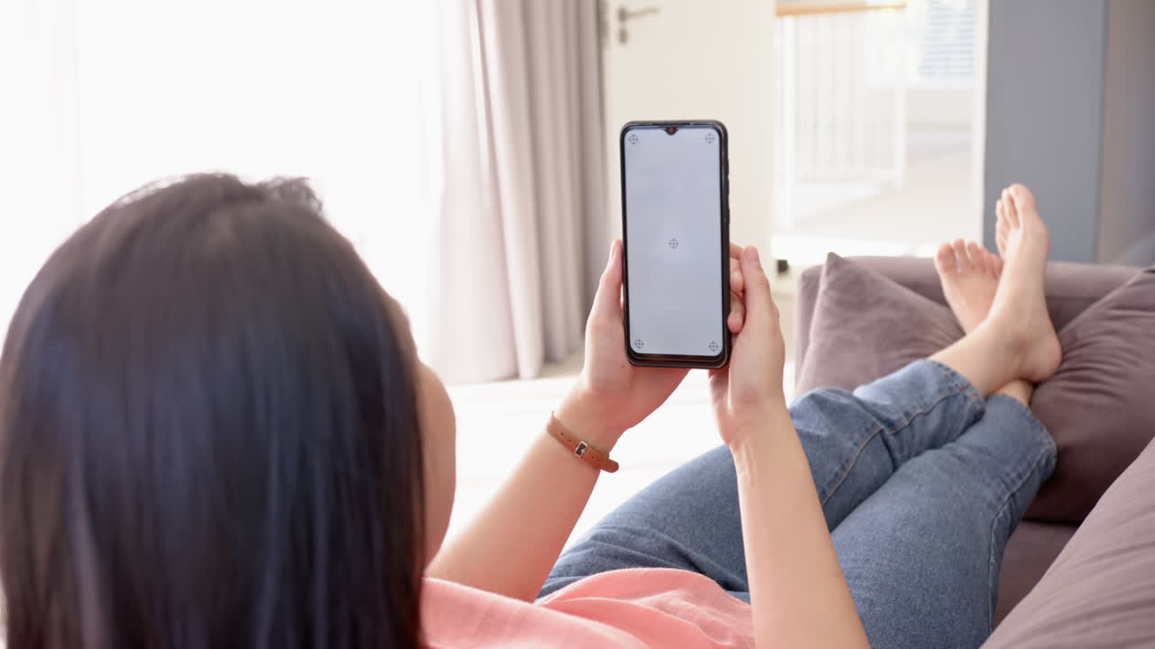 Relaxing on couch, woman holding smartphone and browsing internet at home