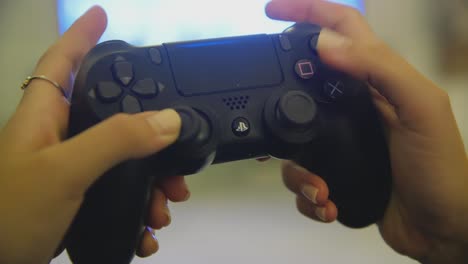 Manos-Femeninas-Usando-El-Controlador-Dualshock-Ps4-Negro-Para-Jugar-Dentro-De-Casa-Con-Tv-En-Segundo-Plano