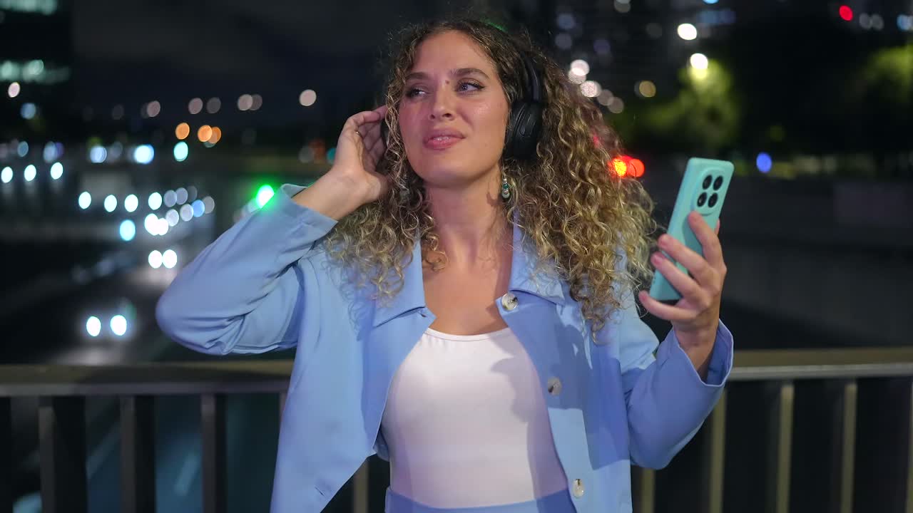 Woman with curly hair listening to music on headphones at night