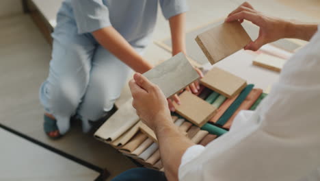 two spouses choose a finish for their home, look at samples of wood, fabric and wallpaper.