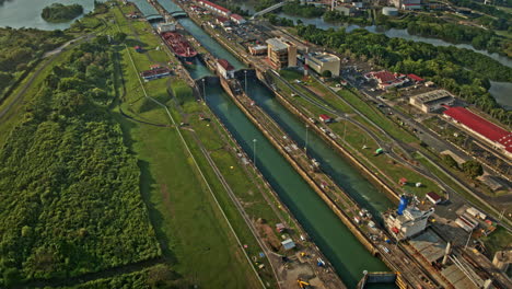 Panama-City-Aerial-v1-hyperlapse-birds-eye-view-overlooking-at-large-cargo-tanker-ship-crossing-miraflores-locks,-tilt-up-reveals-beautiful-landscape-at-sunset---Shot-with-Mavic-3-Cine---March-2022