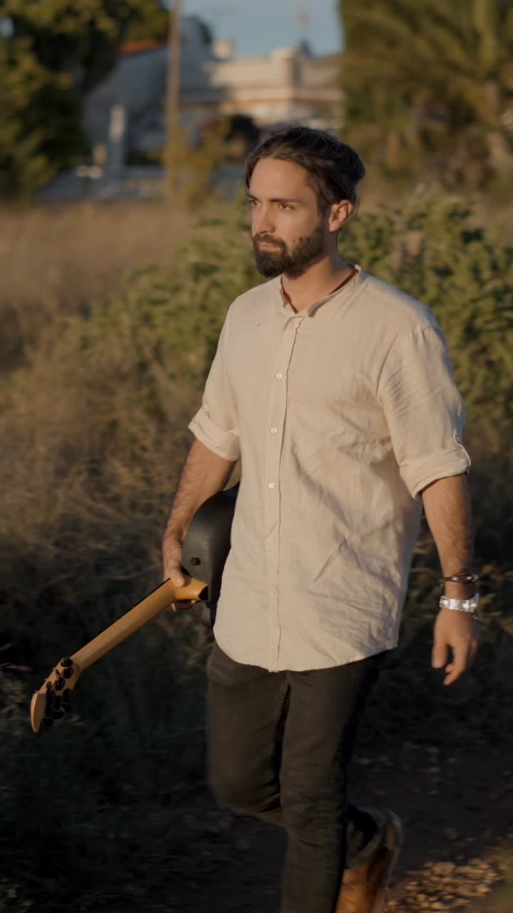 Man walking through a field holding a guitar at golden hour