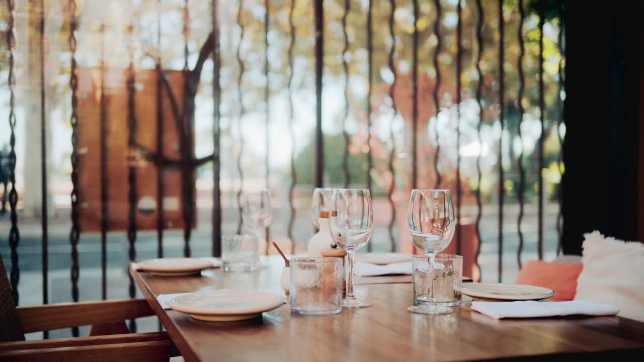 Wooden restaurant table prepared with glasses, plates, and napkins in warm natural light