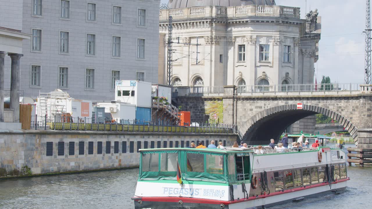 Tour boat with passengers passes historic riverside museum in sunny Berlin, Germany, daytime