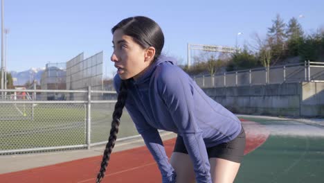 runner woman stops to catch breath with hands on knees on race track, handheld