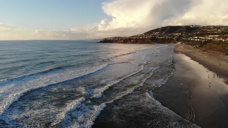 a drone flies high above crashing waves at the beach with a beautiful sky backdrop