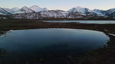 serene twilight view of calm alpine lake and distant snow peaks, aerial