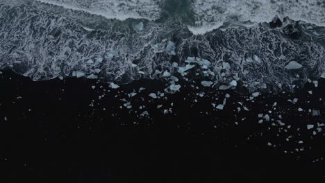 waves with white foam breaking on black sand at diamond beach in iceland