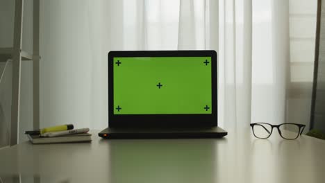 shot of a laptop with chroma key green screen on a table in office room.