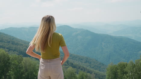 slim woman shakes blonde long hair enjoying highland view