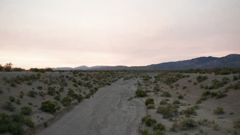 vuelo a baja altura sobre un cauce seco hacia las montañas en el desierto de mojave