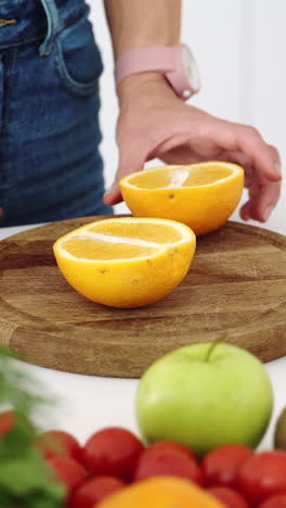 female hands cut with a knife a ripe yellow orange on a wooden kitchen board. vertical video