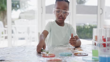 African-american-boy-sitting-at-table-holding-test-tubes-with-liquid,-in-slow-motion