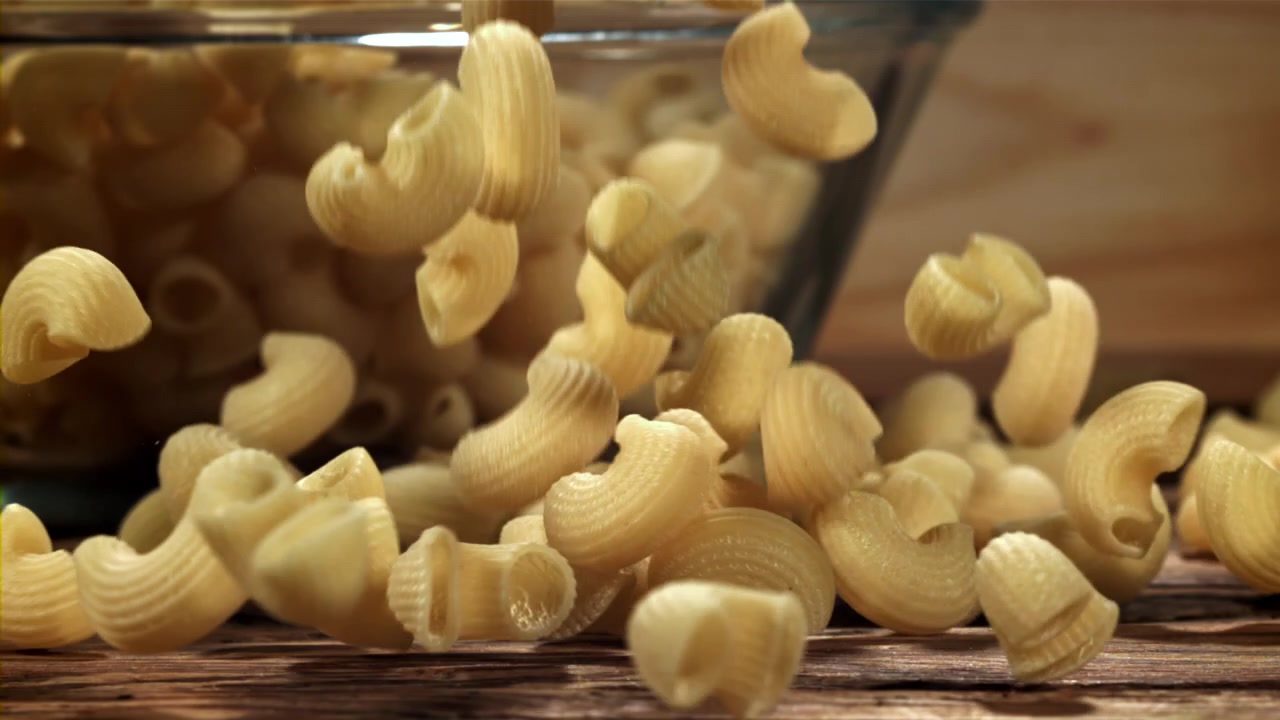 Maccheroni a gomito che cadono su un tavolo di legno al rallentatore