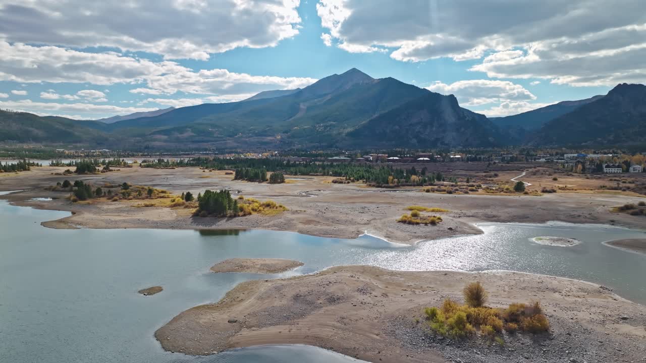 Aerial trucking pan of reservoir with small islands and towering mountains in the background, Colorado