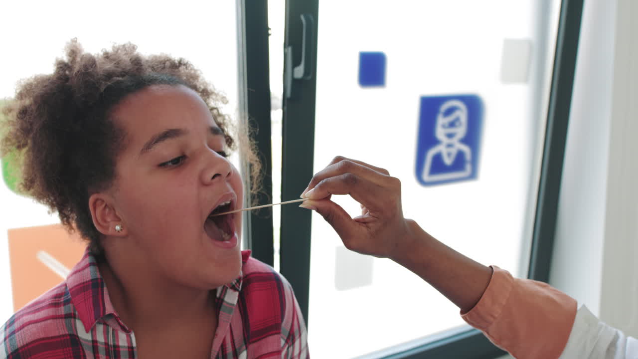 A visit to a child patient by a family doctor pediatrician a girl shows a sore throat to a doctor by