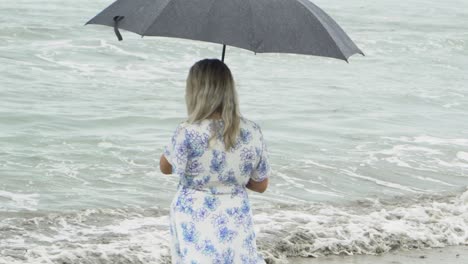 woman walking on beach raining with umbrella