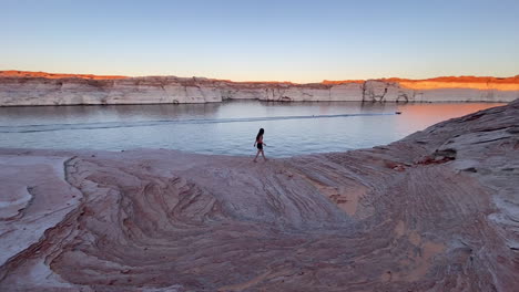 Lonely-Female-Walking-on-Layered-Sandstone-Pattern,-Coast-of-Lake-Powell,-Sunset-Landscape-and-Unique-Texture,-Panorama