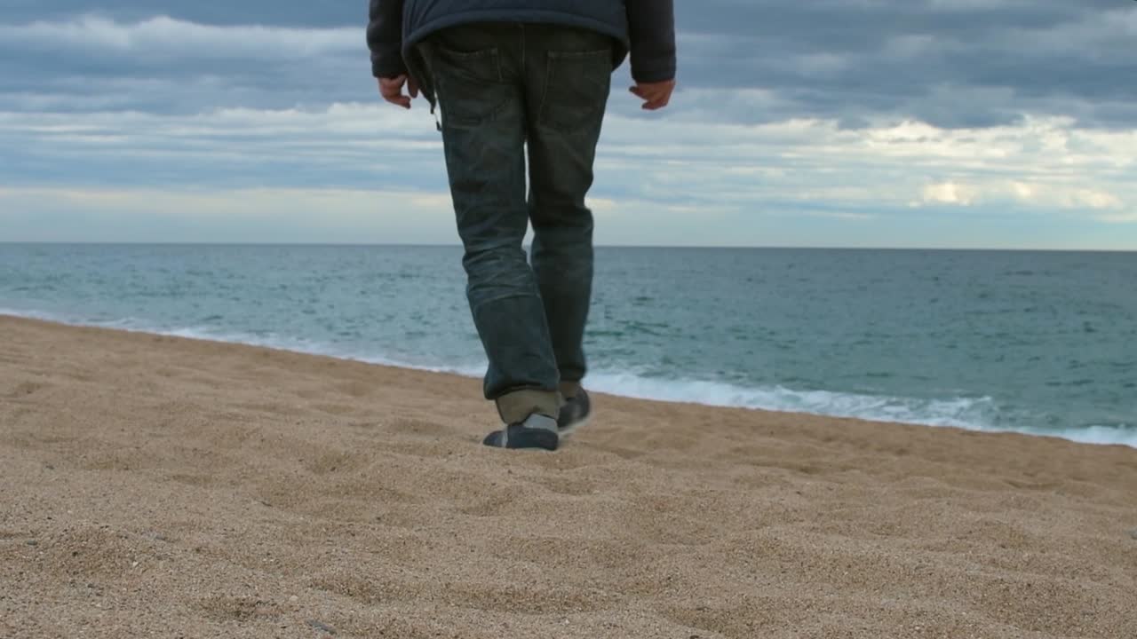 vista de las piernas de un hombre adulto caminando hacia el mar en la playa