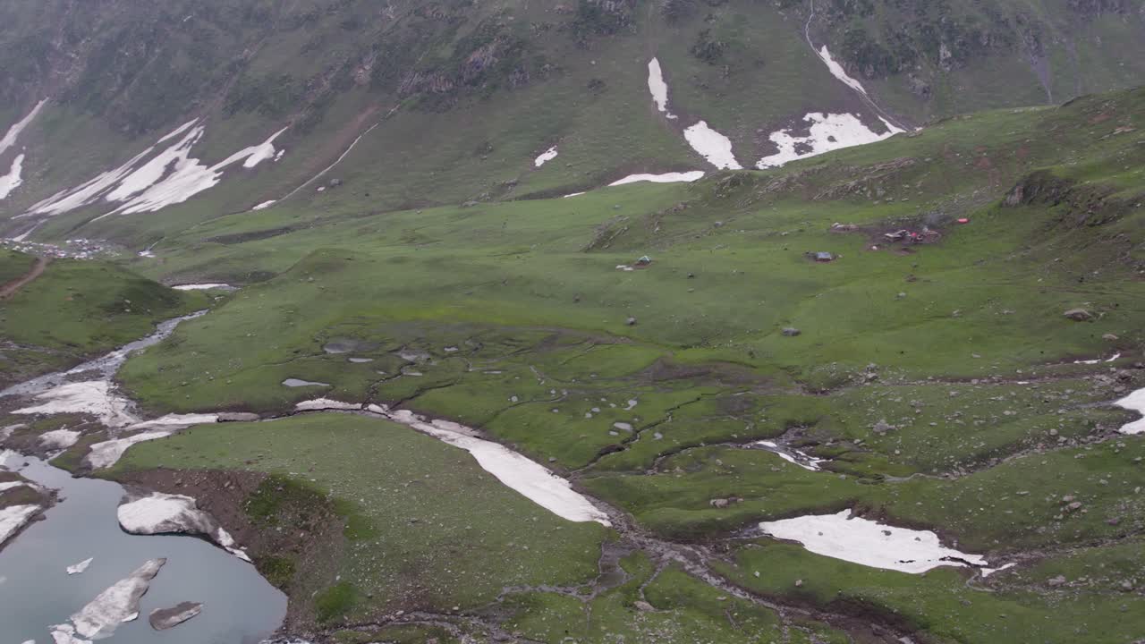 Lush green alpine valley with small streams, rocky terrain, and patches of snow on the hills, in Neelum valley