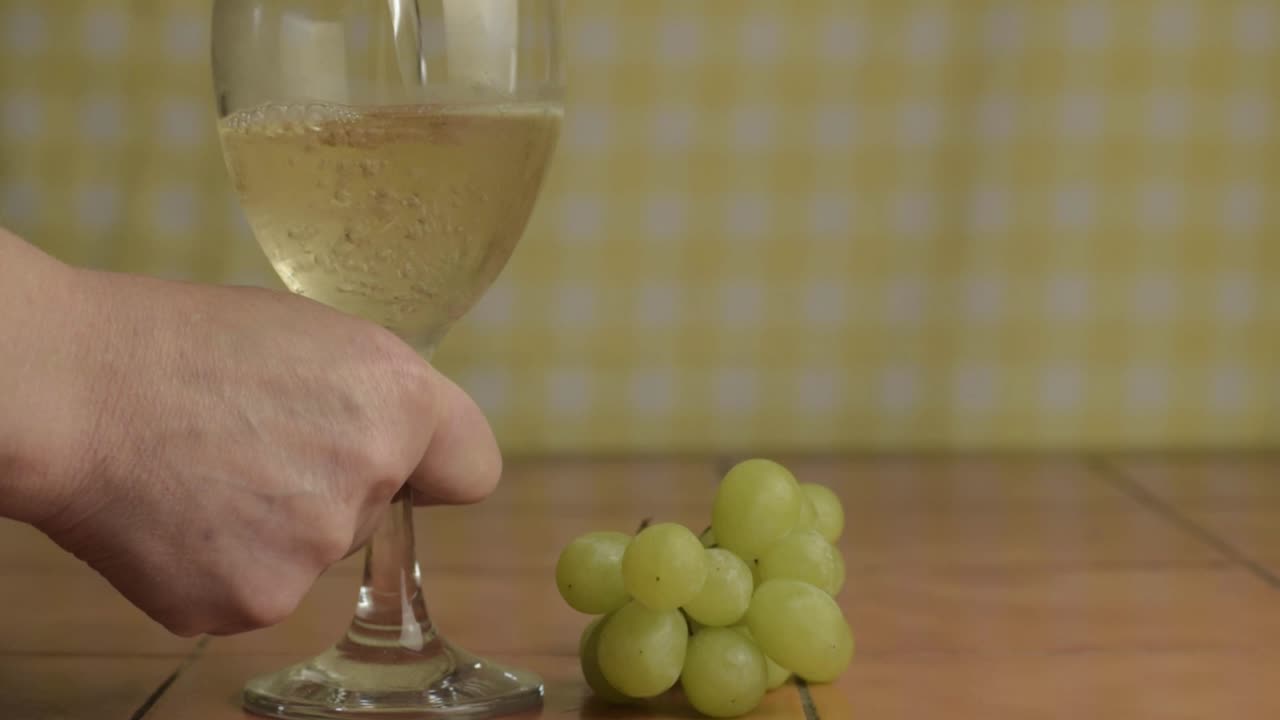 Hand pouring glass of white wine with grapes medium shot