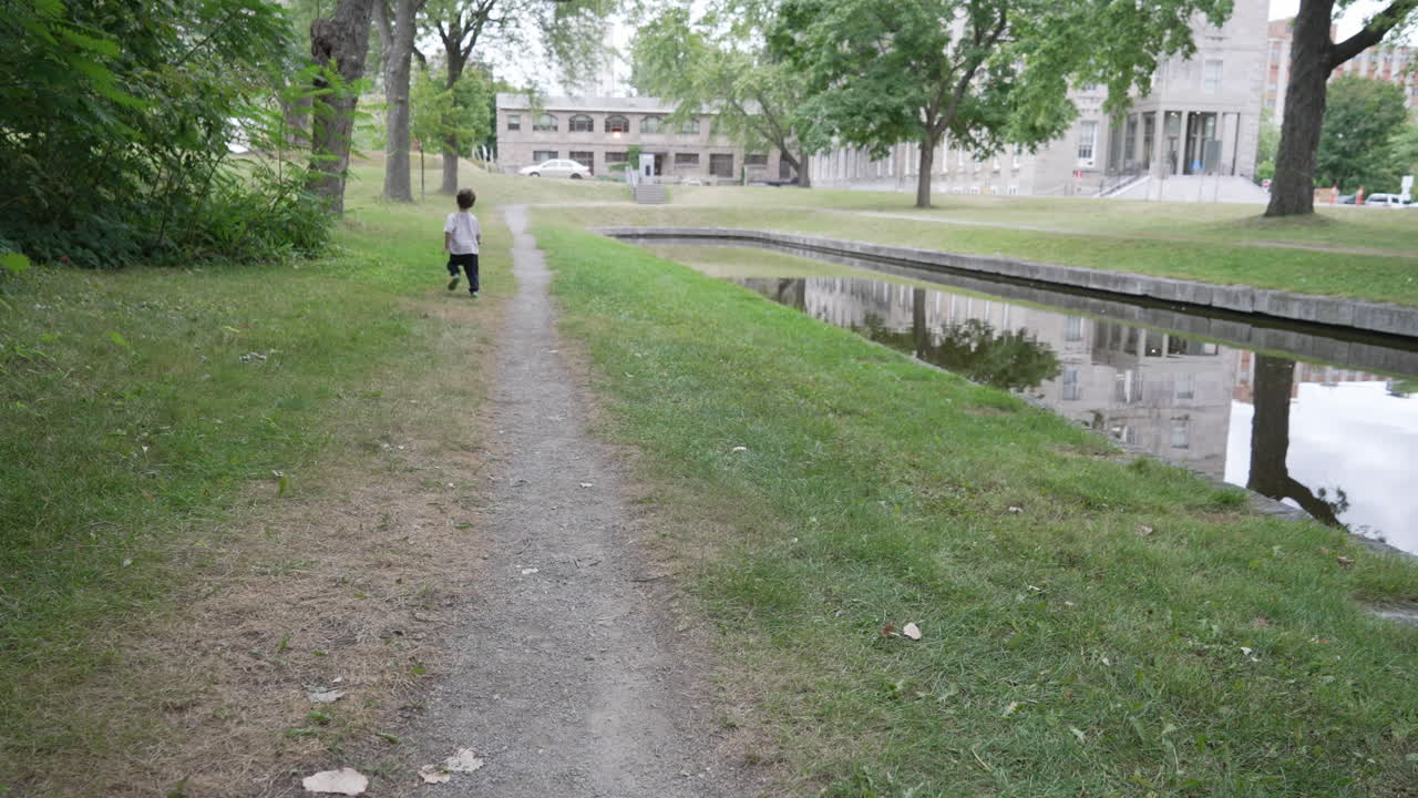 Child running in outdoor garden. Slow motion video of child running at outside home garden. Kid running zig zag with a stick in his hand.