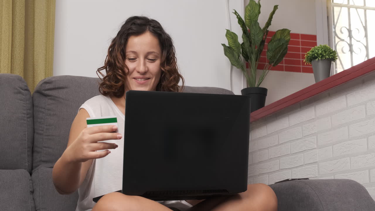 Happy young woman shopping with her credit card and laptop on the couch at home