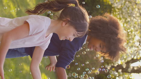 vertical video of smiling boy and girl outdoors having fun playing with bubbles in garden