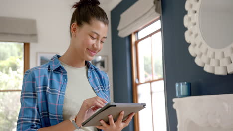 Happy-biracial-teenage-girl-standing-using-tablet-at-home,-copy-space,-slow-motion