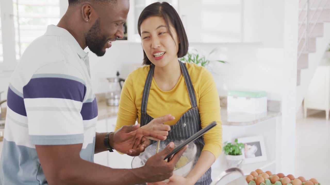 Happy diverse couple wearing apron and baking in kitchen