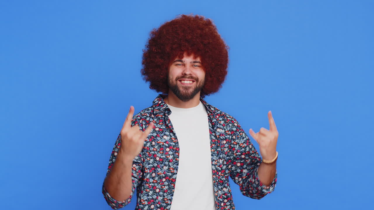 행복하고 즐거운 남자가 록 앤 롤을 보여줍니다. 냉정한 손으로 몸짓, 미친 표정, 춤추며 승리를 얻습니다.