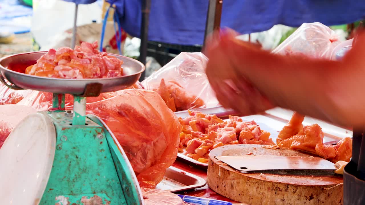 Butcher weighs raw chicken pieces on scale at traditional open-air street market, natural daylight