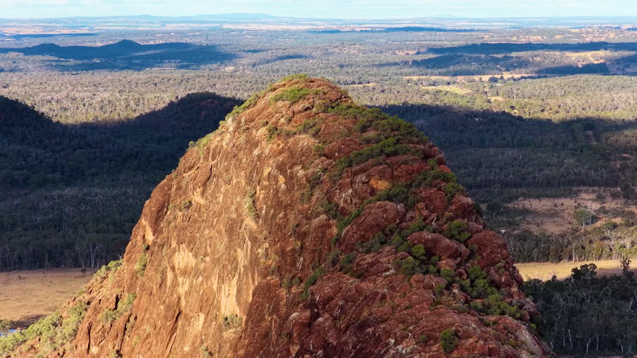 Drone glides over Timor Rock’s rugged volcanic outcrop, golden hour lighting, wide landscape view