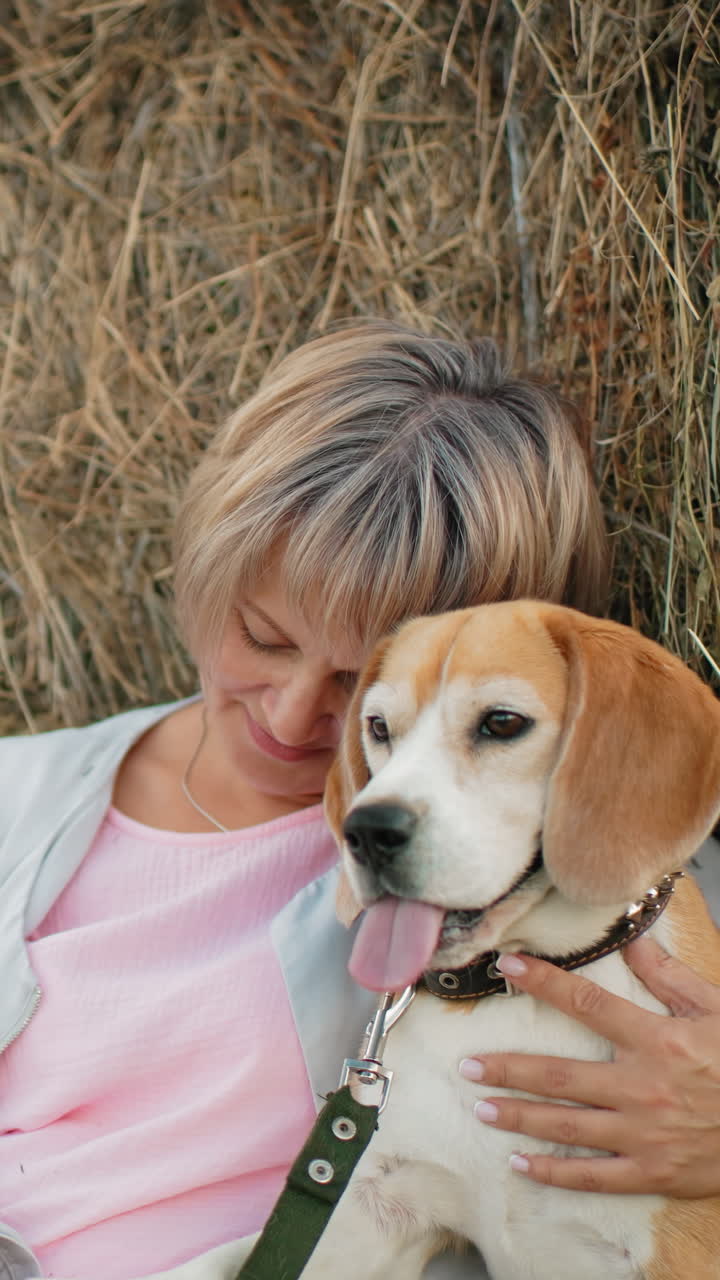 한 여자가 개를 가까이 붙잡고 애정으로 만지며, 광활한 농지에서  에 누워있는 동안, 그녀는 개를 사랑으로 바라보고, 열린 시골에서 평화롭고 친밀한 순간을 공유합니다.