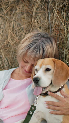 mujer sostiene a su perro estrechamente, tocándolo afectuosamente mientras descansa contra la bala de heno en la vasta tierra de cultivo, ella mira a su perro con amor, compartiendo un momento pacífico e íntimo en el campo abierto