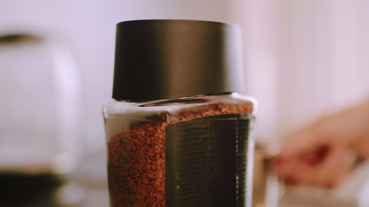 Close up of person opening coffee container on kitchen counter with hand visible, natural light creating soft atmosphere emphasizing morning beverage preparation