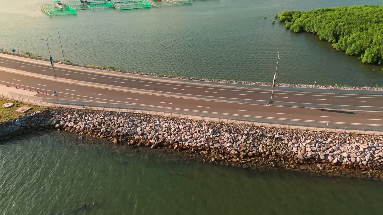 Drone view of vehicles crossing a scenic coastal road in the Philippines, with clear green water and fish pens in the background