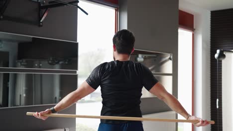 sportsman do shoulder mobility warm up exercise with wooden stick at gym