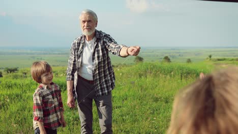 Close-up-view-of-caucasian-senior-man-and-his-grandchildren-playing-with-a-kite-in-the-park-on-a-sunny-day